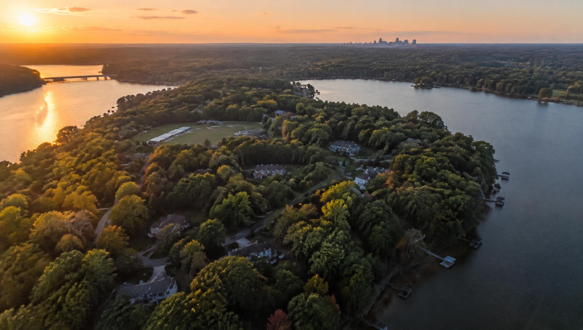 Aerial view at golden hour of the wooded Belmont peninsula between the Catawba River and Lake Wylie, with the Charlotte skyline on the horizon